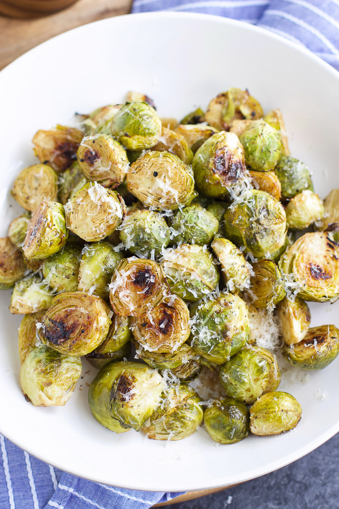 Photo of a large side dish of roasted brussel sprouts with garlic being served with grated cheese on top. 