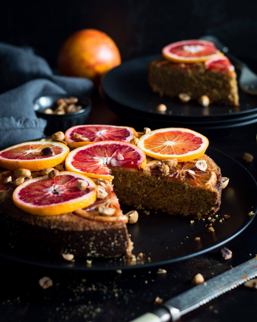 Photo of upside down blood orange cake being served on a dark round plate. 