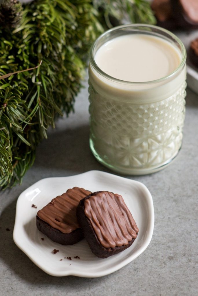 Photo of two vegan chocolate ginger cookies being served with a glass of milk.