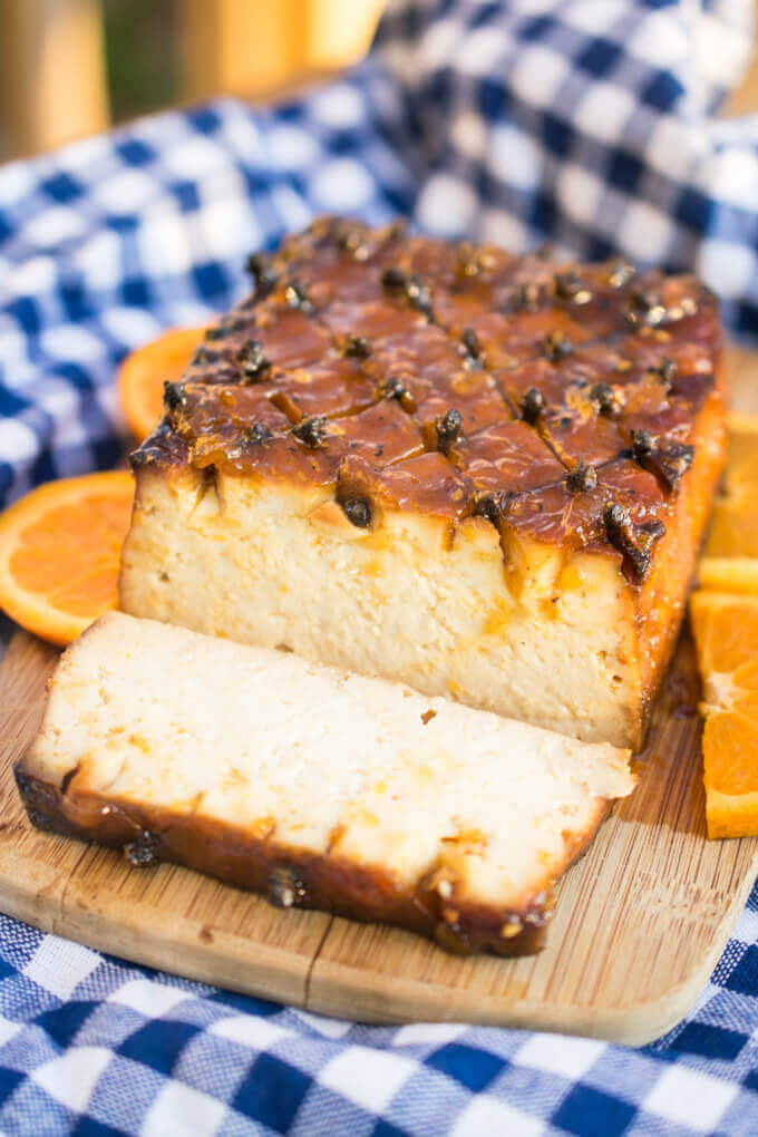Photo of a glazed tofu roast with orange slices and peppercorns as a garnish.