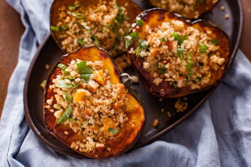 Photo of quinoa stuffed squash with almonds and apricots being served on an oval plate.
