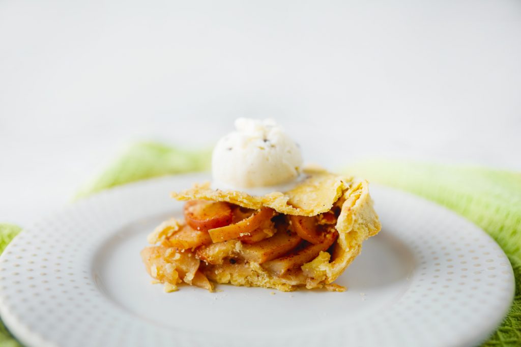 Photo of a slice of grandma's rustic vegan apple pie being served with a scoop of ice cream.