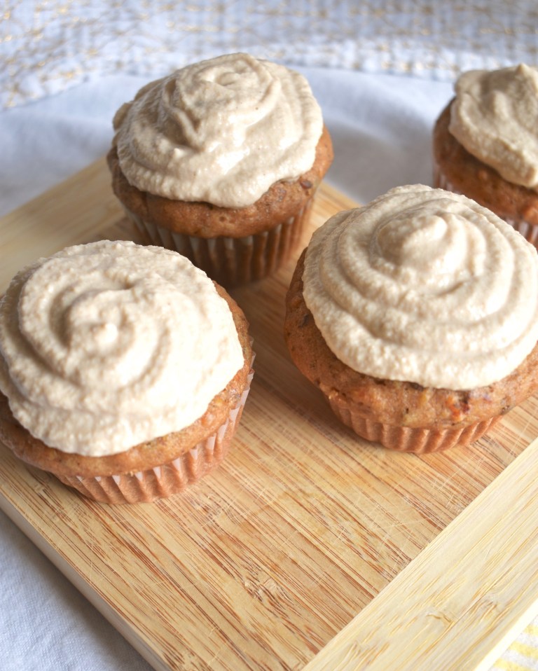 Photo of four carrot cake cupcakes with vegan cashew frosting being served on a wooden board.