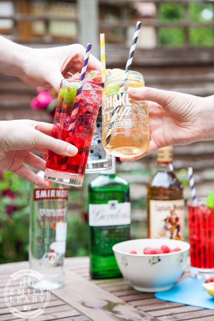 Photo of three glasses clinking together in a cheers with one whiskey ginger cocktail over a table with liquor bottles.