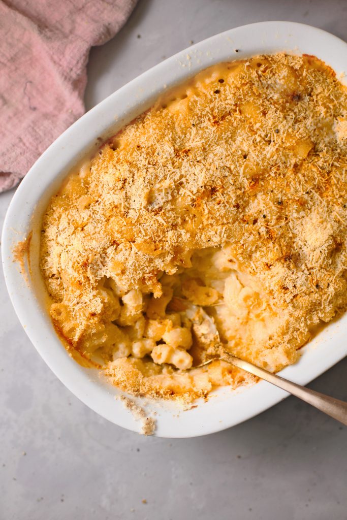 brown breadcrumbs on top of baked vegan mac and cheese that is yellow with a scoop taken out of it with a spoon