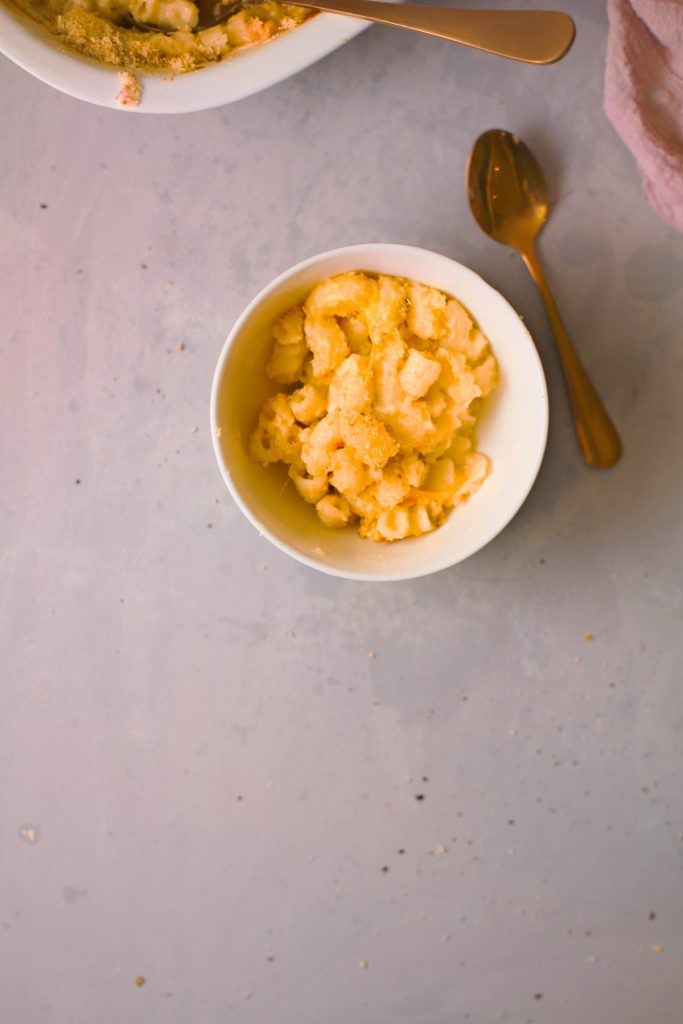 small bowl of yellow pasta with a gold spoon laying next to it on a white table