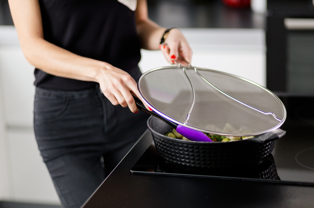 Women using a splatter screen over a frying pan. 