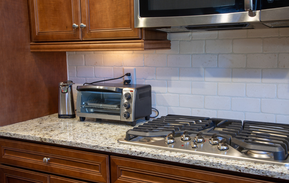 Toaster oven sitting on the kitchen counter under the cabinets.