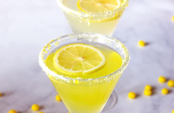 Photo of two bright yellow candied martini lemon cocktails with a lemon slice garnish and salt on the rim.