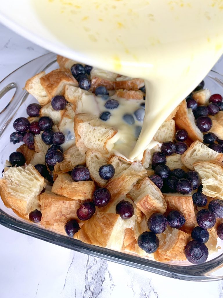 sauce being poured over blueberry bread pudding