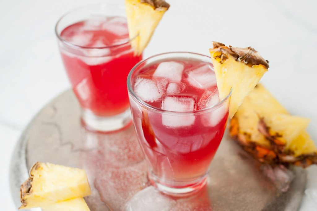 Photo of two malibu bay breeze cocktails being served over ice with a pineapple garnish.