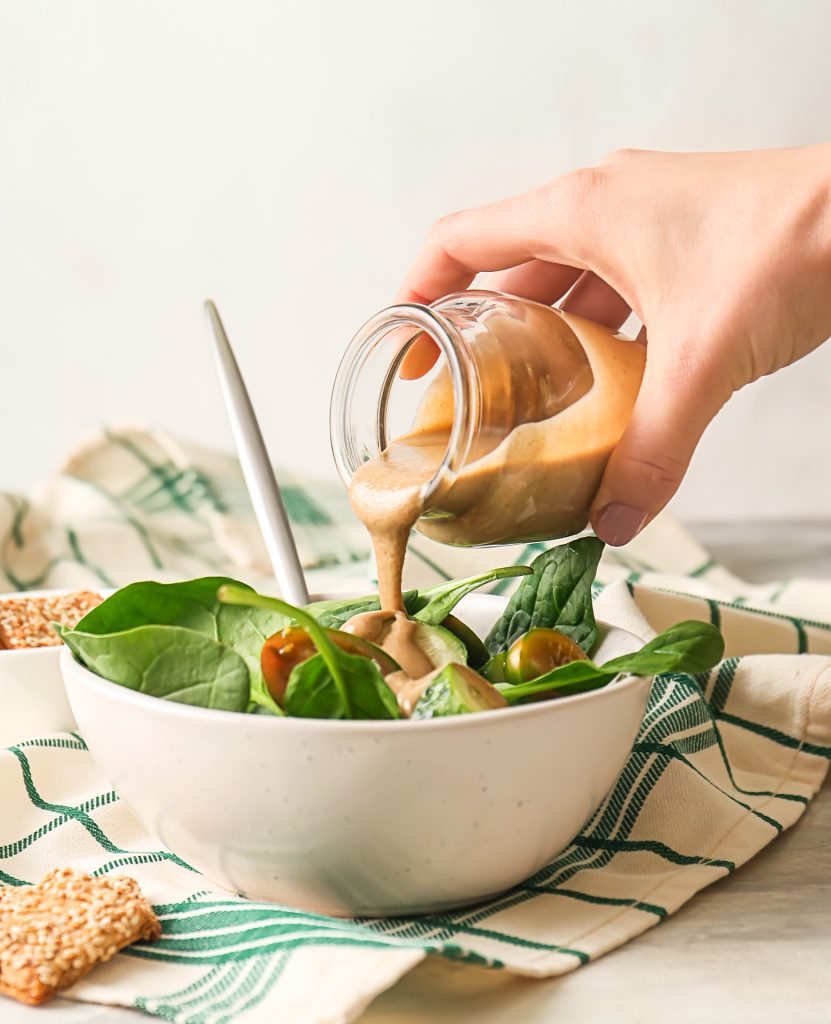 maple tahini dressing being poured onto salad