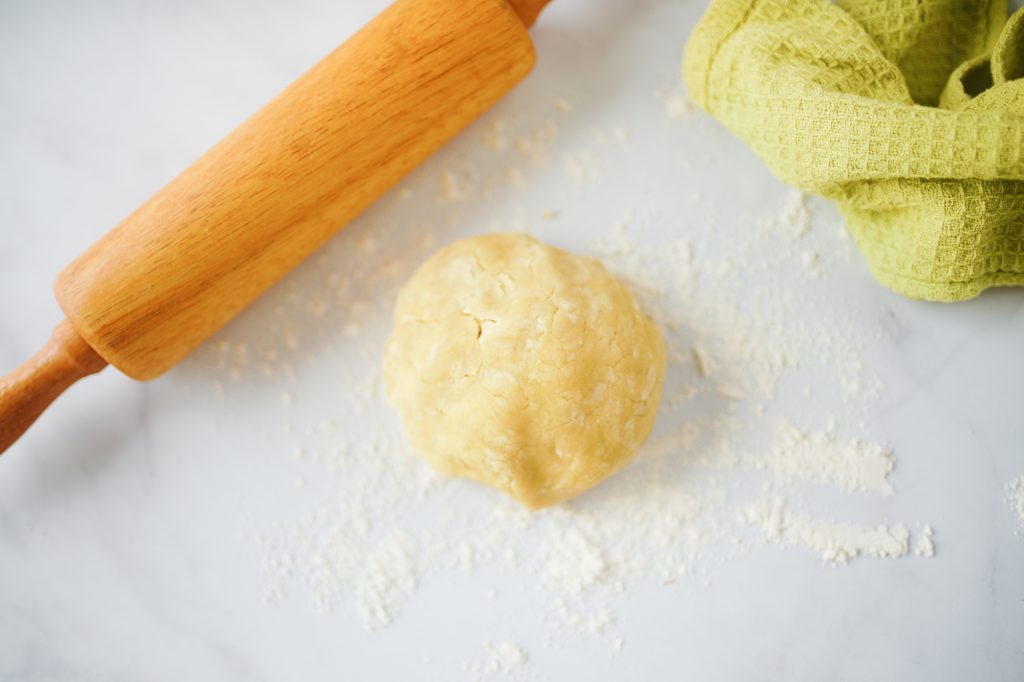 Flat lay of pie dough in a ball with rolling pin and dish towel
