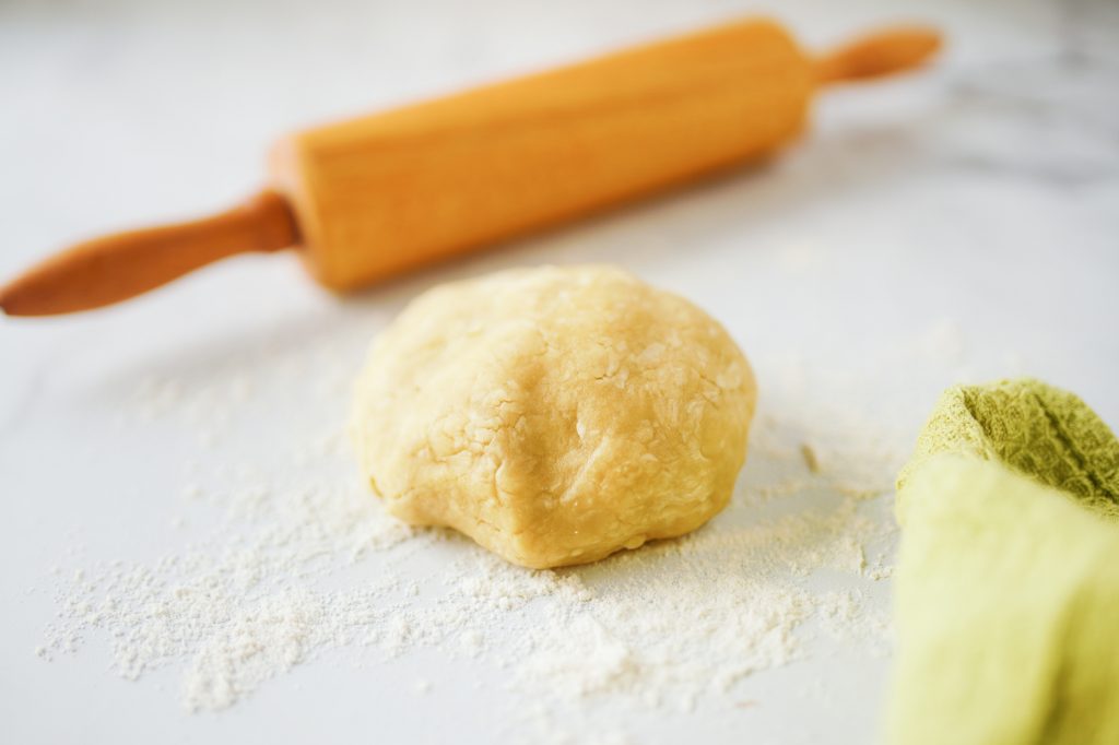 close up photo of pie crust in a ball with rolling pin