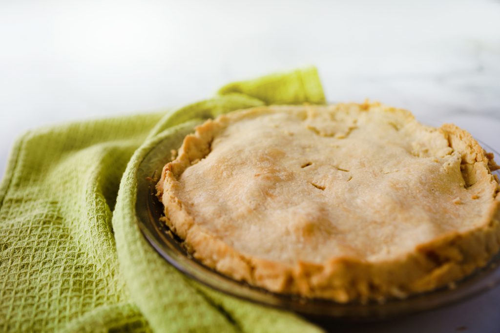 A finished apple pie in glass pan next to green towel.