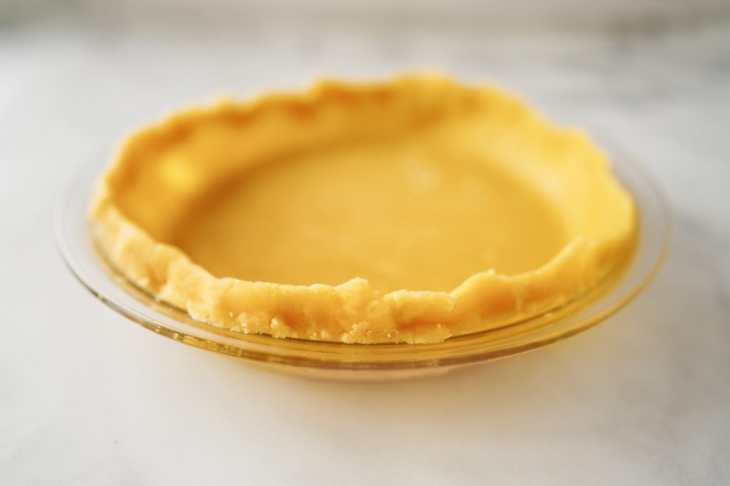 Close up of front side of oil pie crust in a glass pan on marble counter.