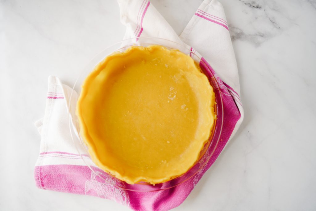 Flatlay of oil pie crust dough in pan with purple towel on marble counter.