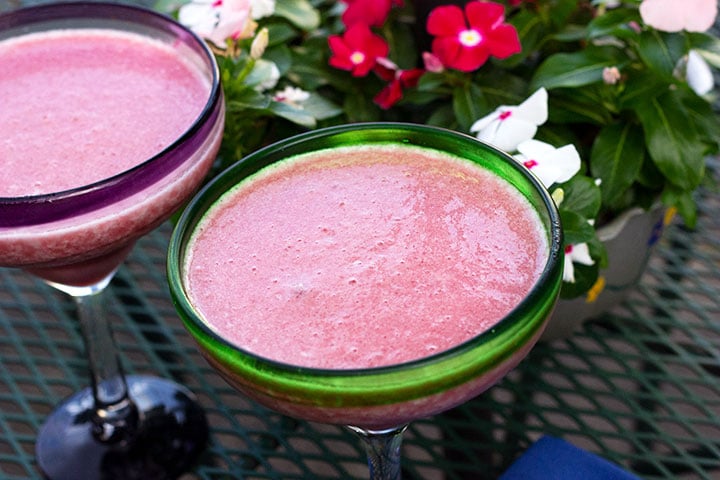 Looking down into two margarita glasses serving pineapple margaritas with raspberry sauce. 