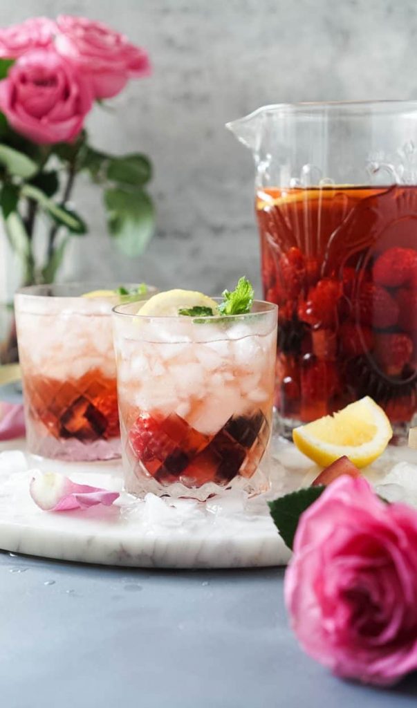 Photo of rose sangria in a large pitcher, also seen are two glasses filled with rose sangria and a garnish of lemon.