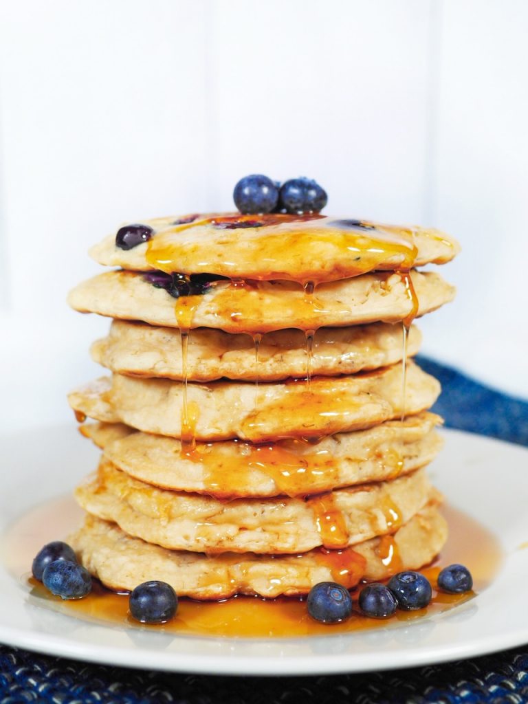 close up photo of vegan blueberry pancakes on plate with maple syrup and fruit