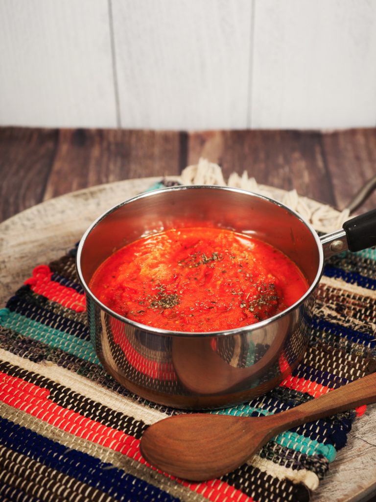 red vegan tomato sauce in small sauce pan on top of a place mat on a brown board