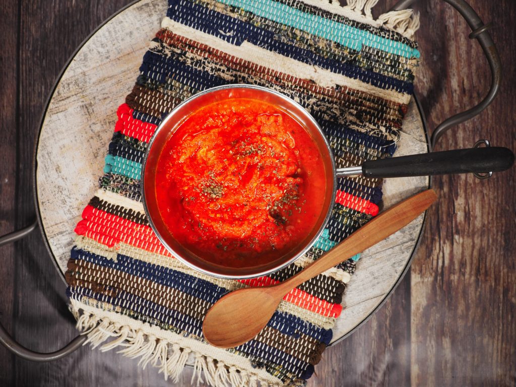 vegan marinara sauce in pan from above with a brown wooden spoon laying down next to it. 