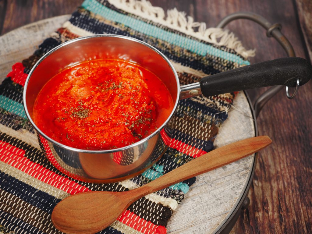 spoon laying next to red colored vegan tomato pasta sauce in pan on top of placemat