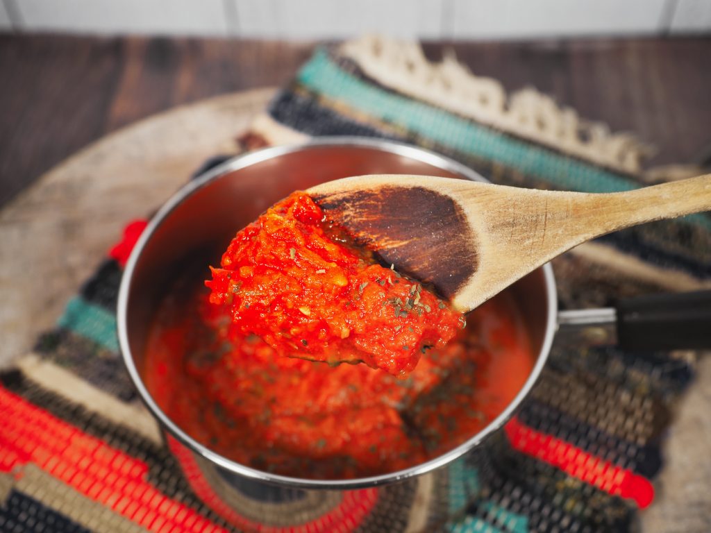 spoon scooping up red vegan tomato sauce with a little multi colored place mat 