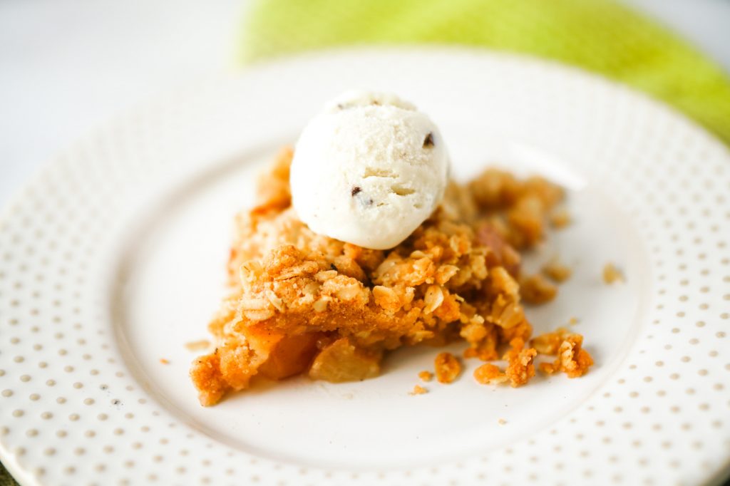 Photo of a small serving of vegan apple crisp with ice cream on top. 