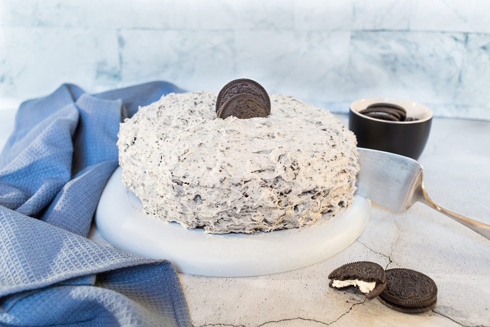 Photo of vegan Oreo cake with buttercream frosting being served on a round white platter. 