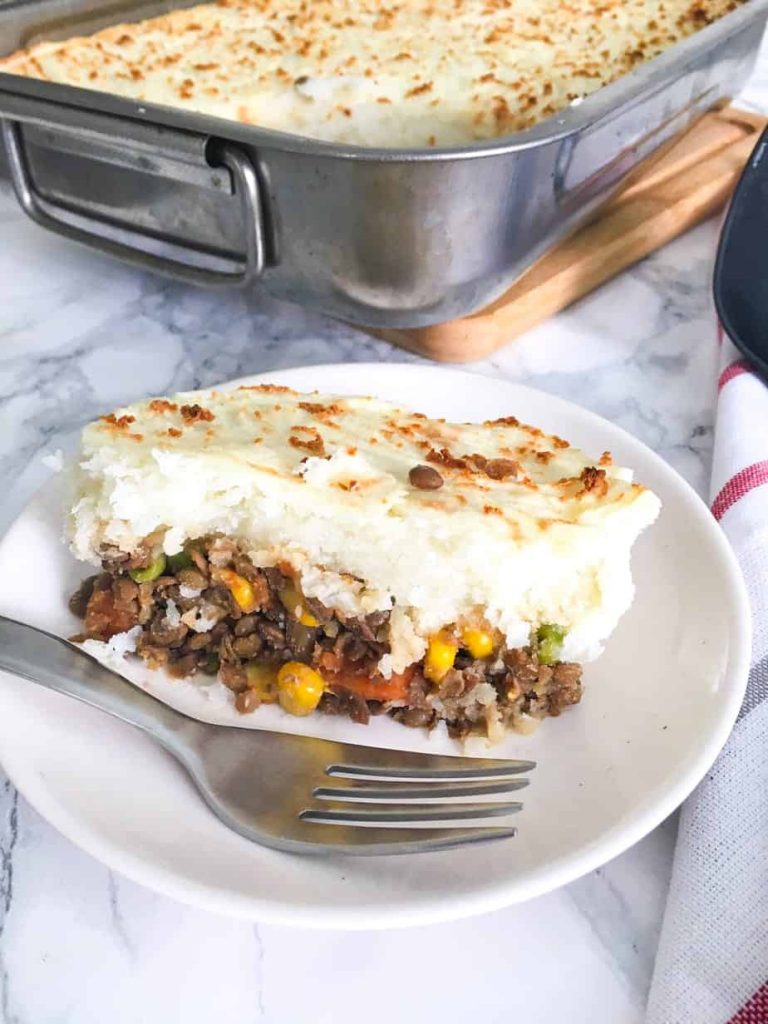 Photo of lentil shepherd's pie being served on a small round white plate. One of the classic and comforting vegan Thanksgiving recipes. 