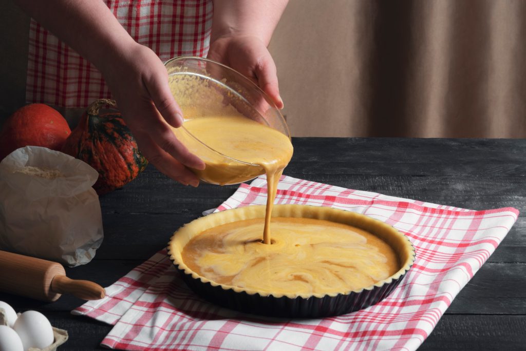 Photo of a person pouring pie filling into a pie dish with a pie crust. 