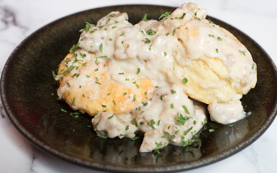 Photo of southern-style vegan biscuits and gravy being served on a dark round plate. One of the ultimate in comfort food vegan Thanksgiving recipes. 