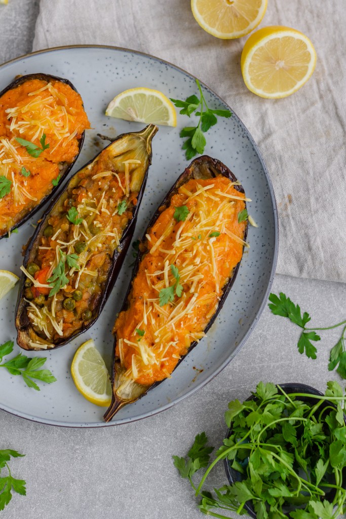 Photo of vegan lentil shepherd's pie stuffed eggplant being served on a speckled round plate. 