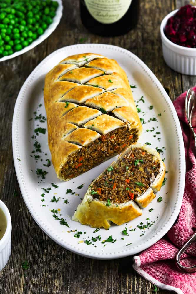 Photo of the ultimate vegan wellington sliced and being served on a white oval platter. 