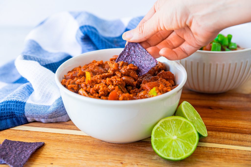 tortilla chip being dipped into easy vegan chili recipe in bowl