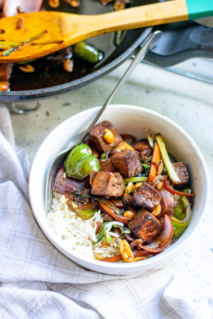 bowl of vegan kung pao with pot behind it