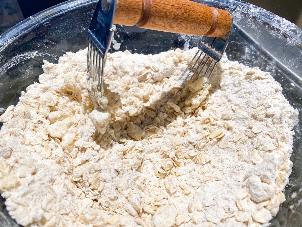 cutting butter for oat crumb topping in a clear bowl