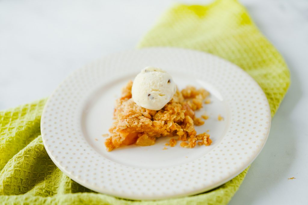 ice cream on top of vegan apple crumble recipe on white plate sitting on top of green dish towel