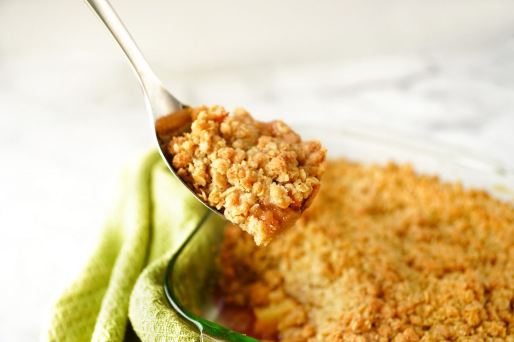 vegan apple crisp on serving spoon with green dish cloth in the background