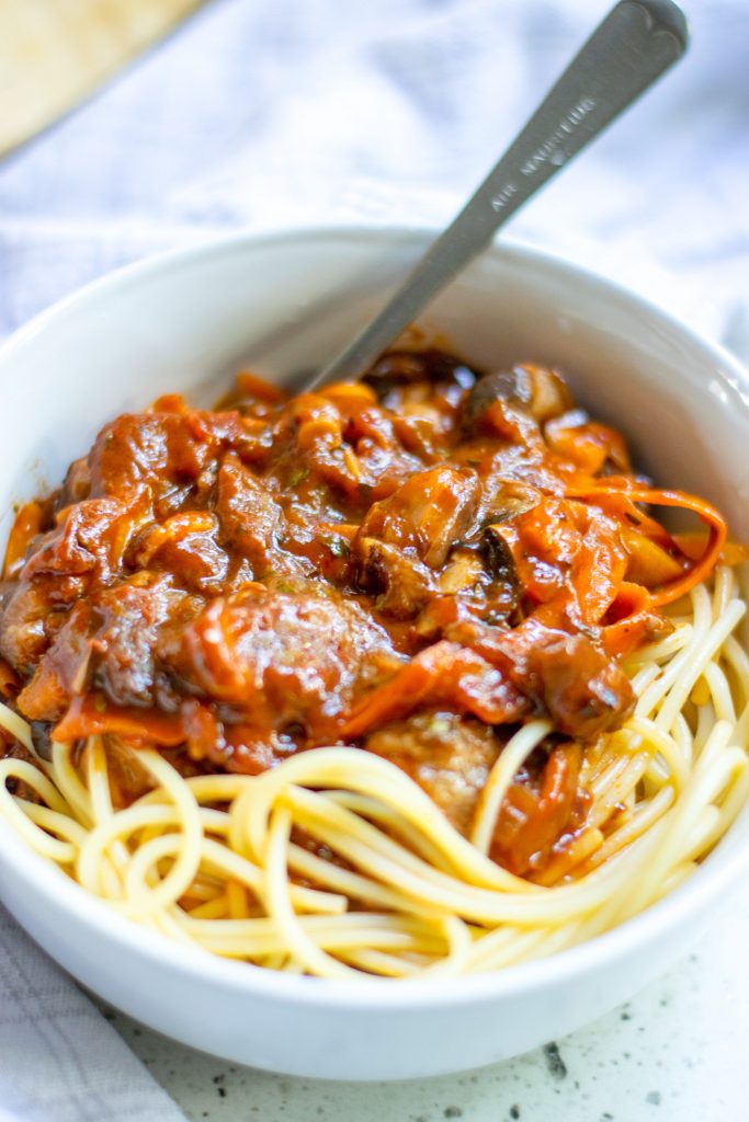 close up photo of vegan bolognese over pasta noodles in bowl with mushrooms