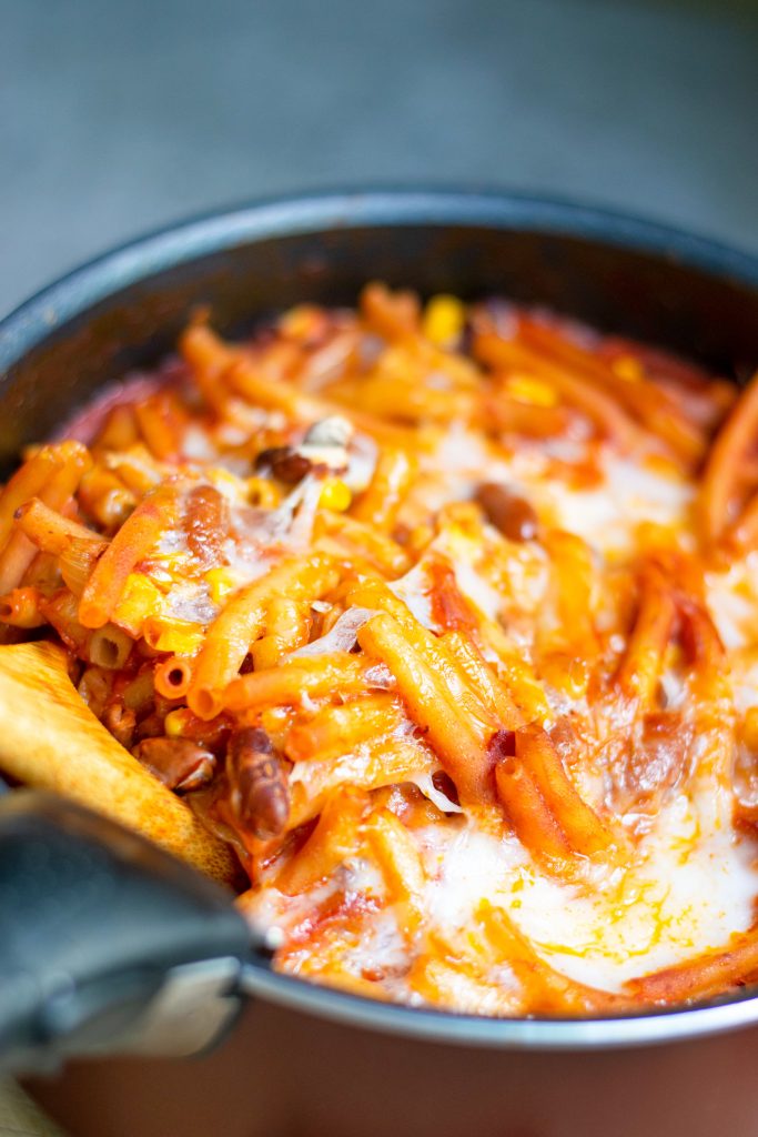 close up of one pot vegan chili mac being scooped out of baking dish