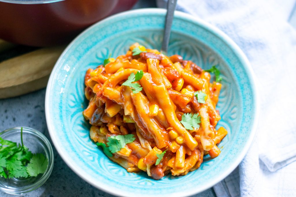 vegan chili mac in blue bowl with spoon and cilantor