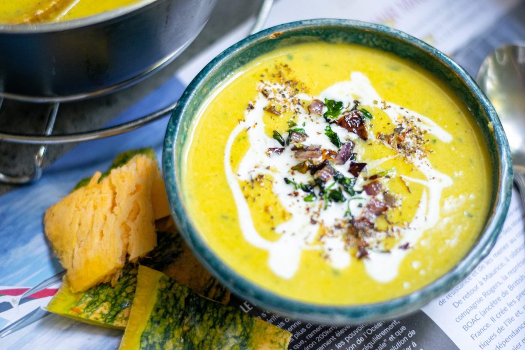 orange color vegan pumpkin soup without coconut milk in a blue bowl with pumpkin on the table