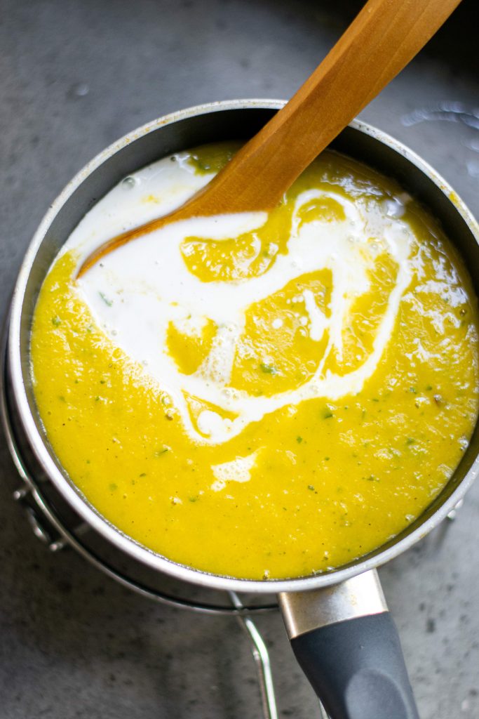 yellow vegan pumpkin soup finished in pot being stirred with coconut milk swirled in