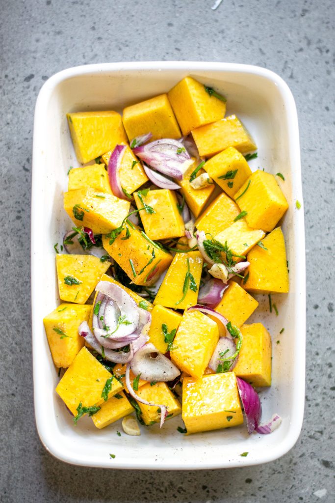 pumpkin for roasting with onions and garlic in a white baking dish