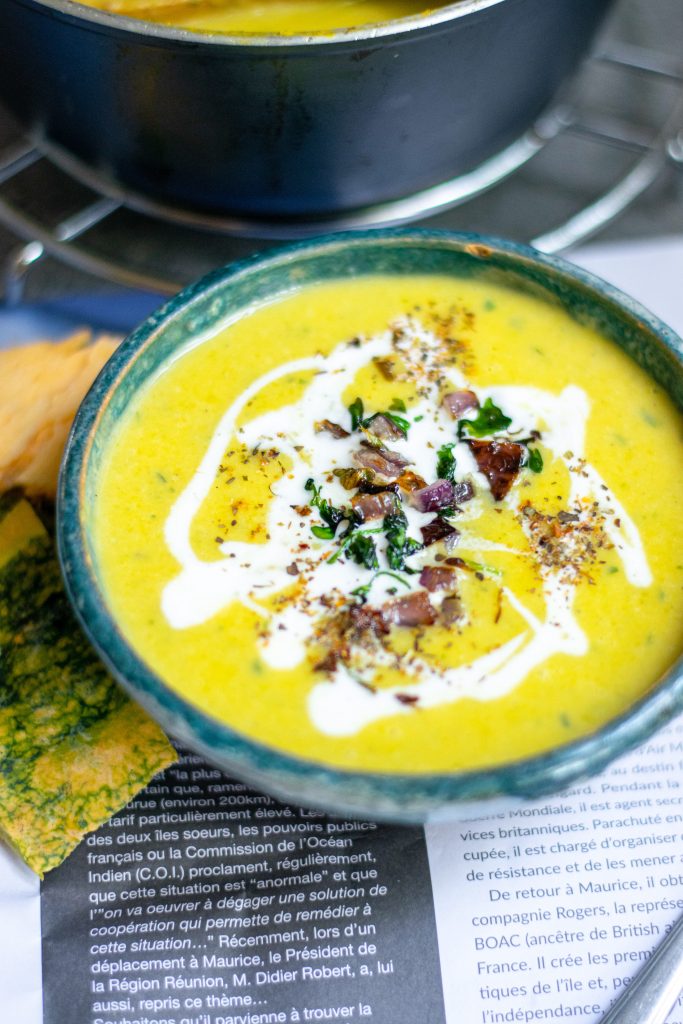 side view of yellow soup with white cream on it in a blue bowl