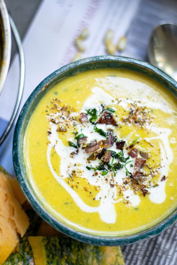 spoon on the side of vegan pumpkin soup with coconut milk swirled in on a blue bowl