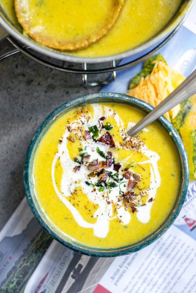 orange color vegan pumpkin soup with crispy onions and garlic on top of paper 