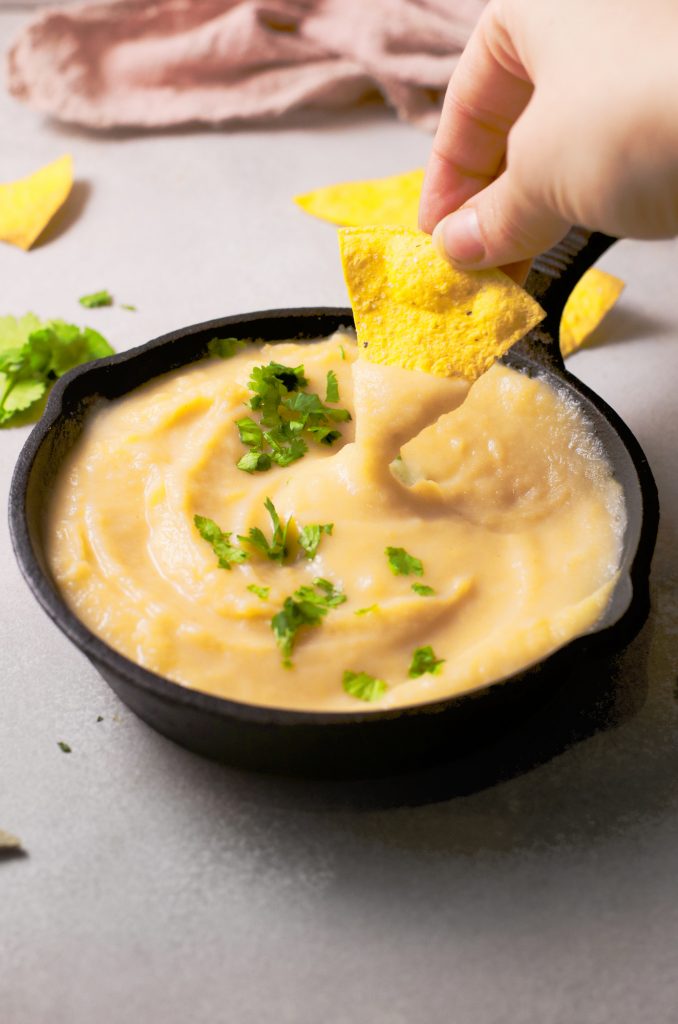 hand dipping chip into vegan queso recipe